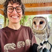A person smiling into the camera with a masked owl on a falconry glove